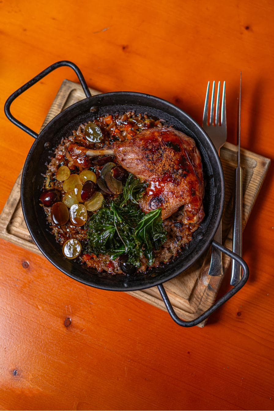 Arroz de pato no forno do Mãe Restaurante, servido em tacho de ferro com uvas e couve crocante