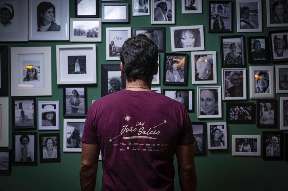 O chef João Diogo Saloio de costas, diante da parede de fotografias de mães e avós do Mãe Restaurante, em Lisboa