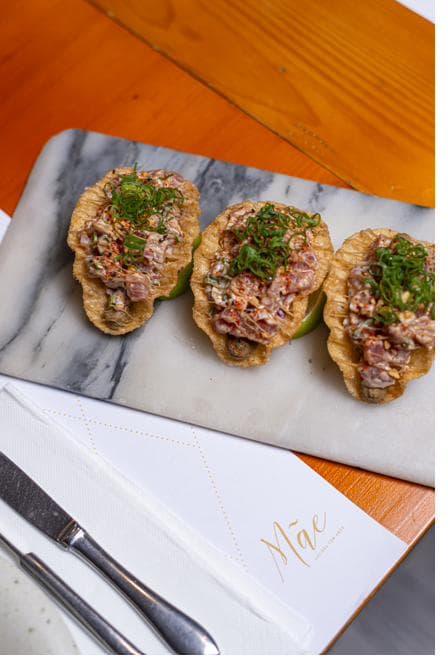 Três tacos de atum fresco servidos sobre tábua de mármore
